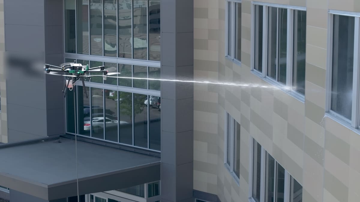 One of our green-deck hexacopters fires a long, straight jet of water toward the upper windows of a tan and glass building.